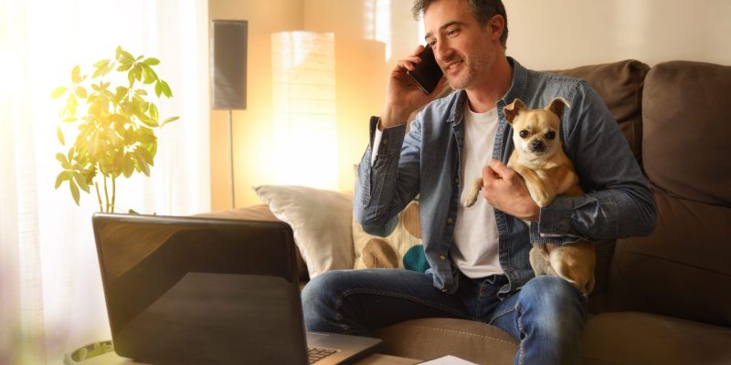 Man working from home talking on the phone with his dog in his arms in a warm environment.